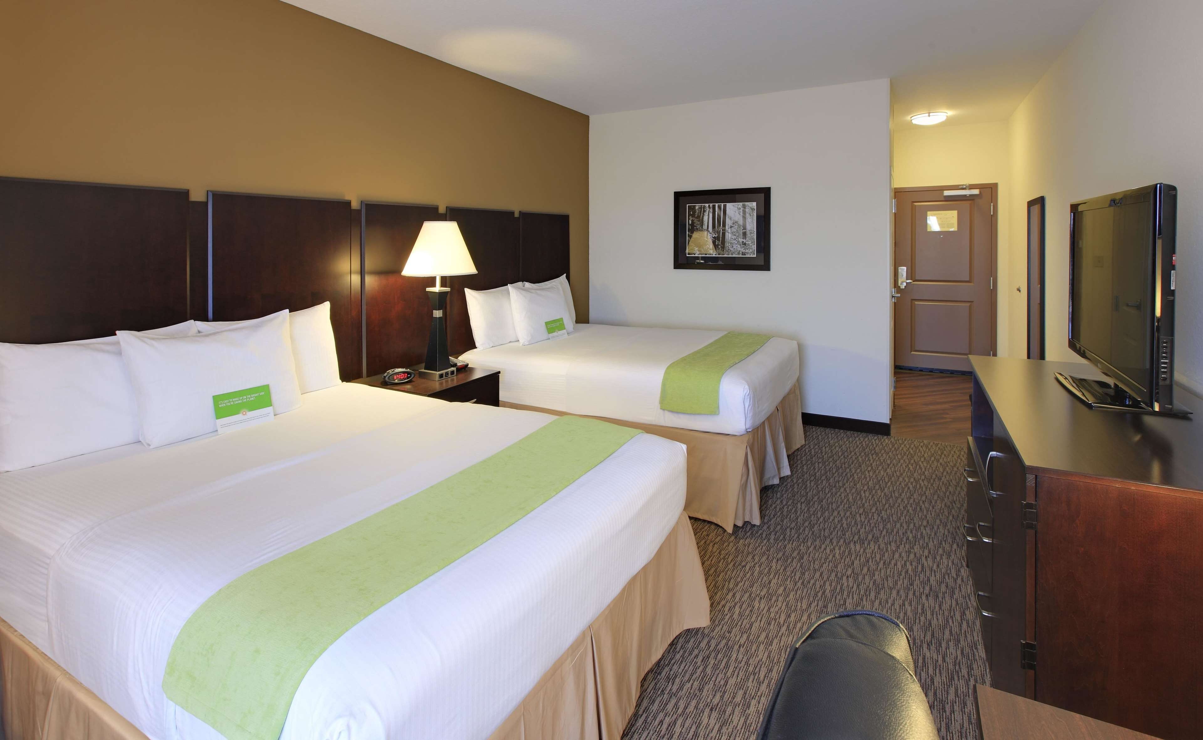 A hotel room with two beds, a desk, a television, and a framed picture on the wall.