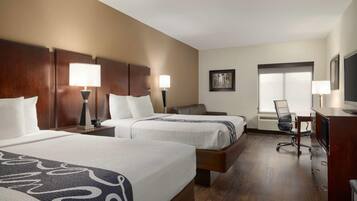 A hotel room with two beds, a desk, a chair, and a television.