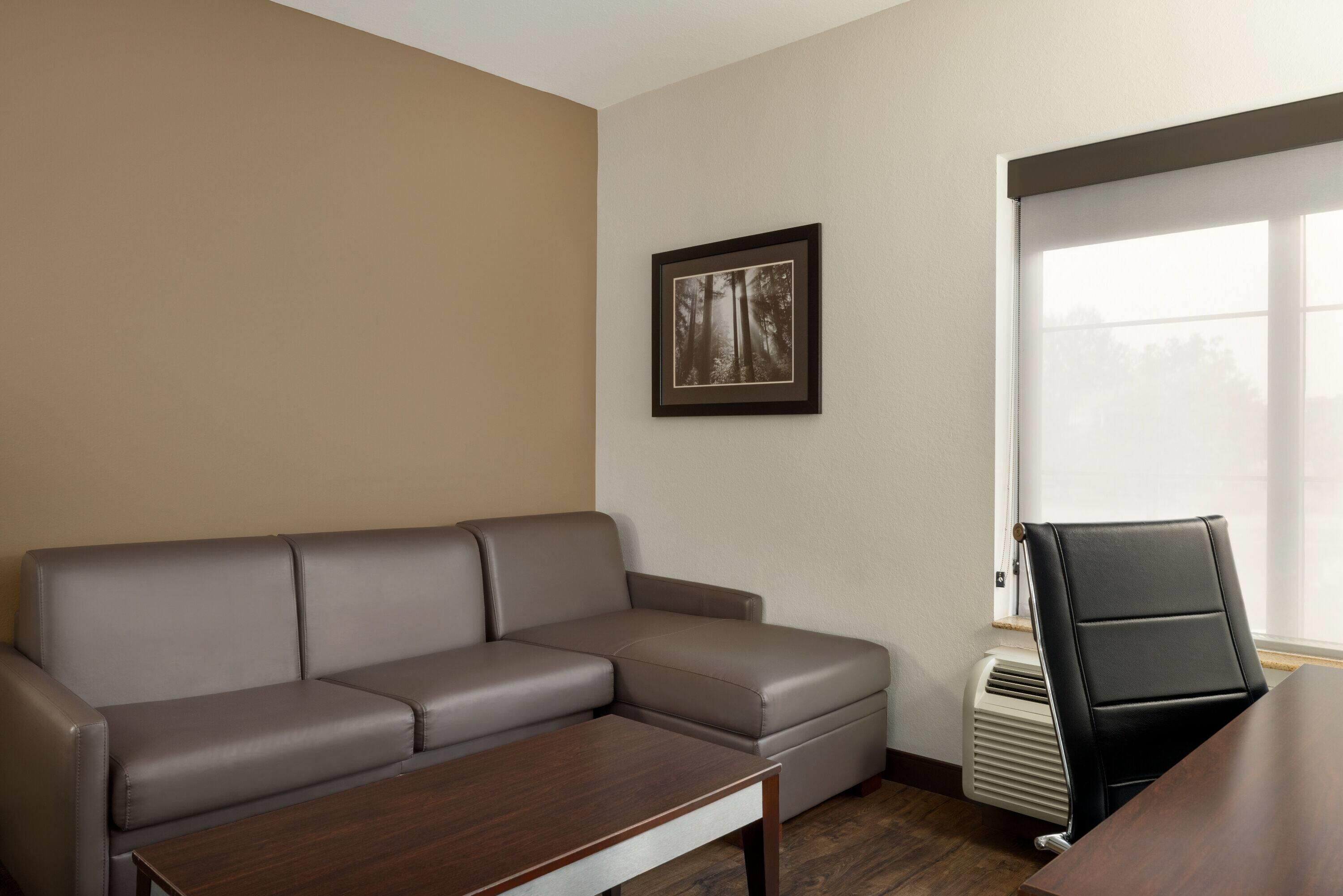 A room with a gray leather sofa, a wooden coffee table, a framed picture on the wall, and a window with blinds.