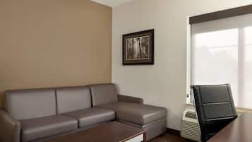 Una habitación con un sofá de cuero gris, una mesa de centro de madera, un cuadro en la pared y una ventana con persianas.