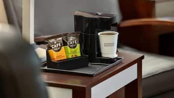 Una cafetera, dos cápsulas de café y una taza con la etiqueta 'Wyndham Rewards' sobre una mesa de madera en una habitación de hotel.