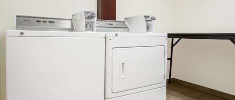Una lavadora blanca y compacta en un espacio reducido, con piso de baldosas y puerta de madera.
