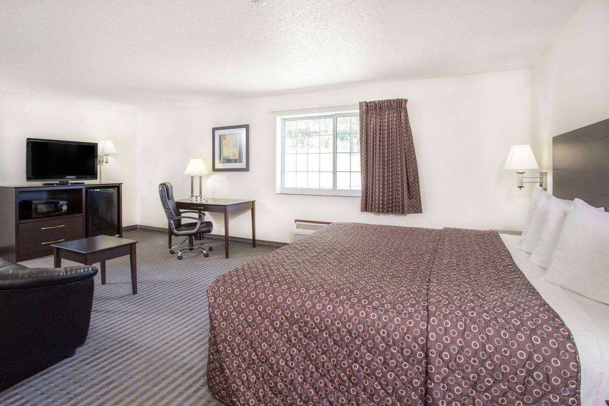 A hotel room with a bed, a desk, a chair, a television, and a window with curtains.