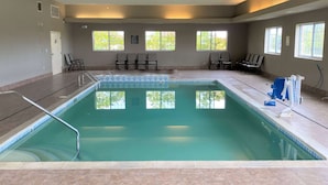 Una piscina interior con agua cristalina, rodeada de sillas y un suelo de baldosas.