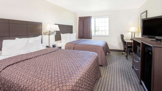 Habitación de hotel con dos camas, un escritorio, un televisor y una ventana con cortinas.