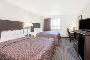 A hotel room with two beds, a desk, a television, and a window with curtains.