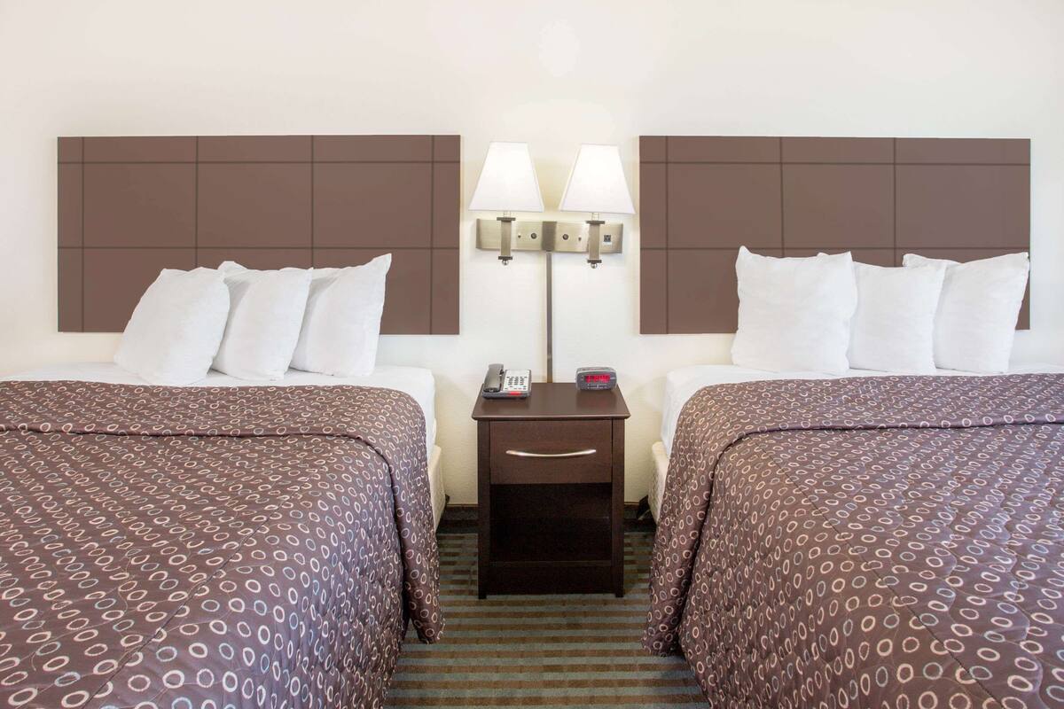 A hotel room with two beds, a nightstand with a lamp, and a telephone.
