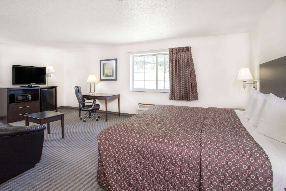 A hotel room with a bed, a desk, a chair, a television, and a window with curtains.