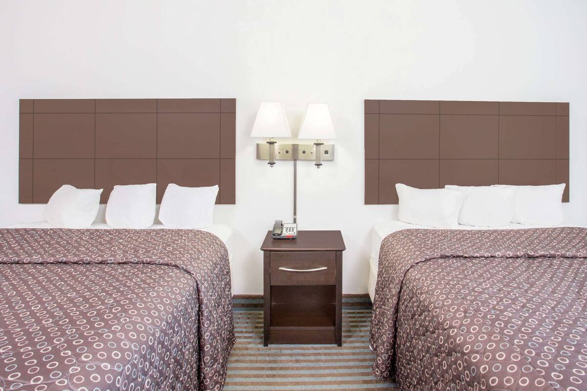 A hotel room with two beds, a nightstand with a lamp, and a telephone.