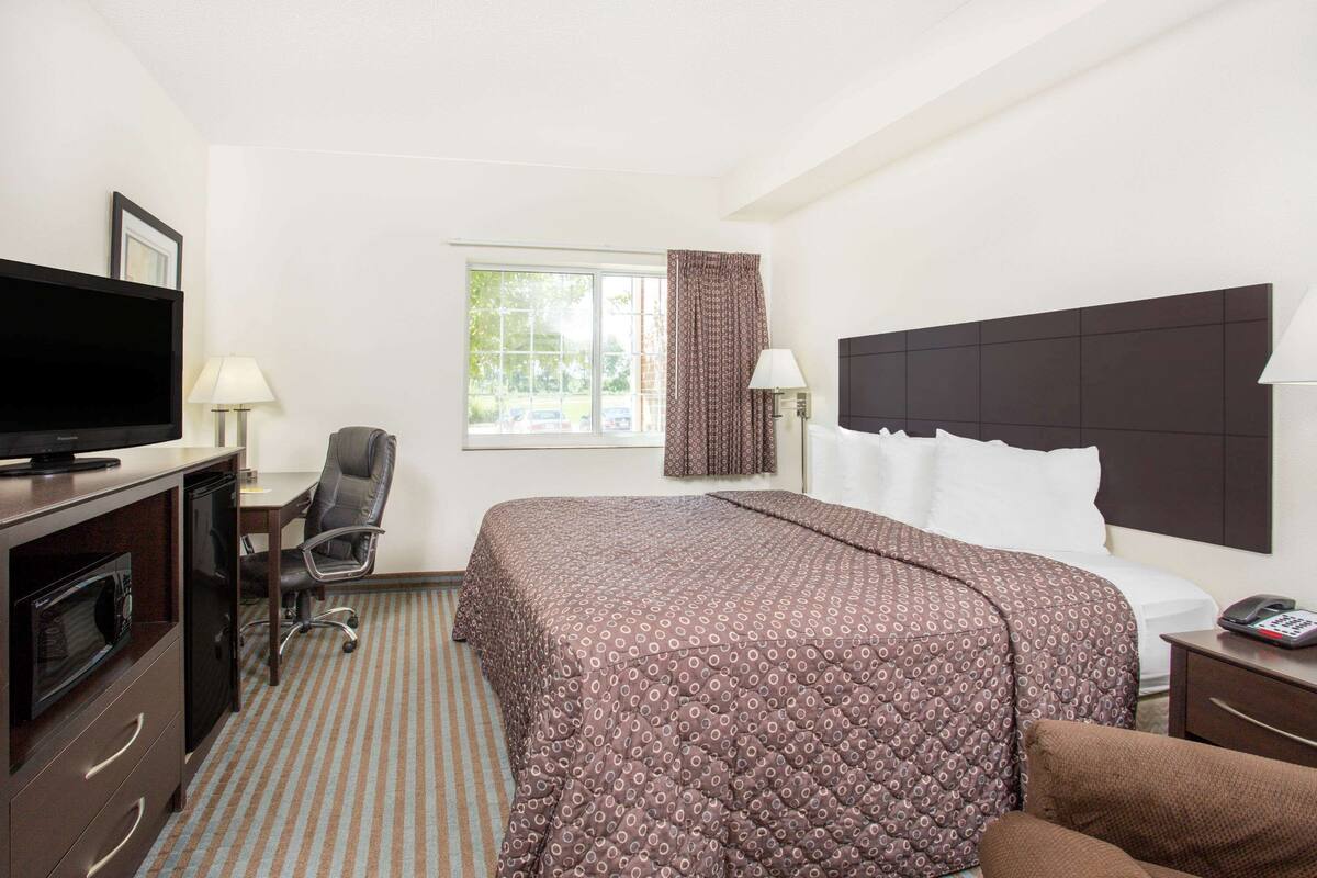 A hotel room with a bed, a desk, a television, a chair, and a window with curtains.