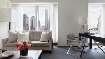 A modern living room with a sofa, a coffee table with books, a vase of flowers, and a desk with a lamp.