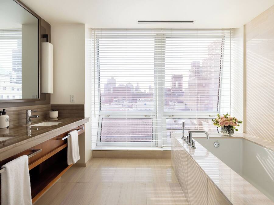 A modern bathroom with a large window, a bathtub, and a vanity with a mirror.