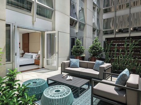 A modern outdoor seating area with a sofa, armchairs, and ottomans, a glass door leading to a bedroom, and potted plants.