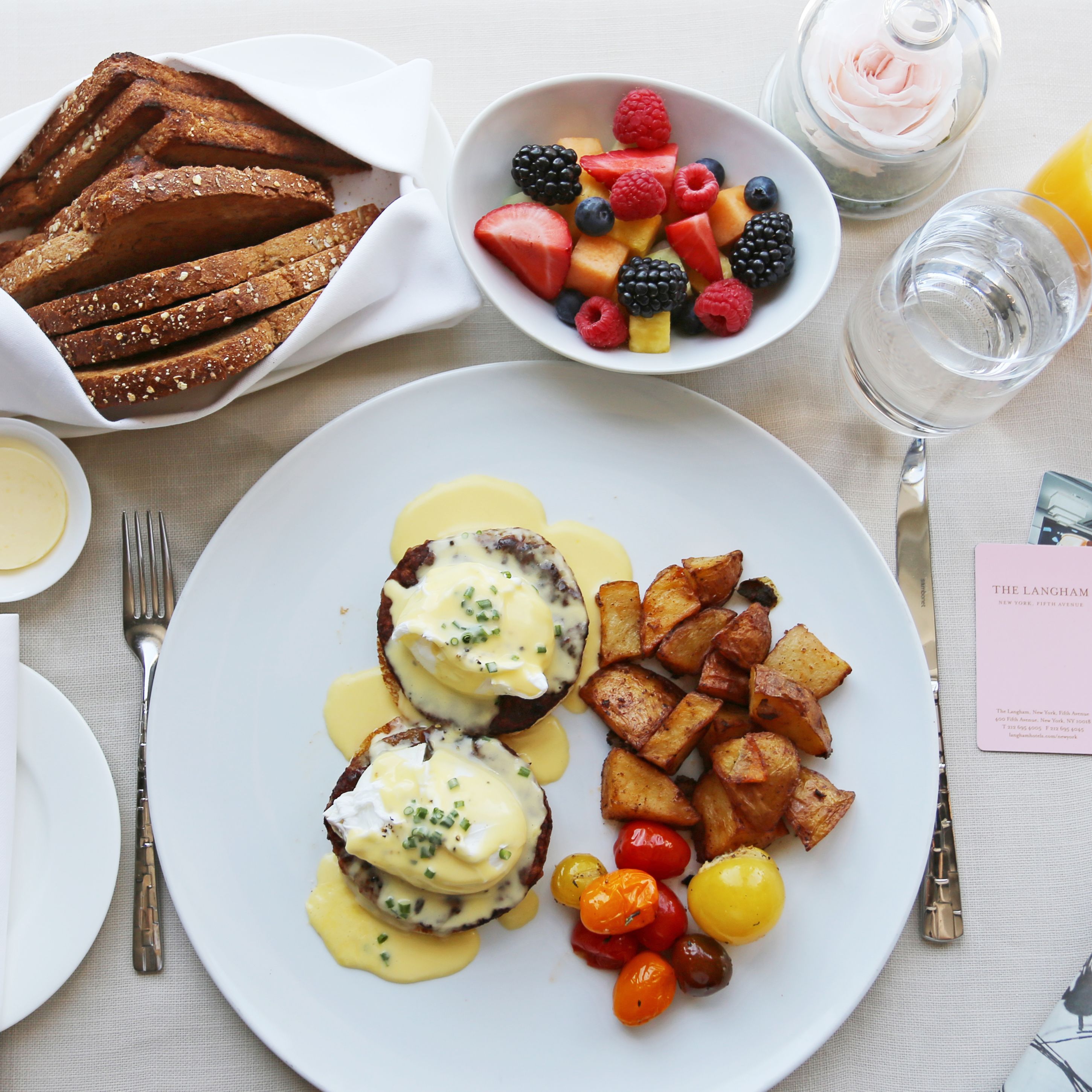 Un desayuno con huevos Benedictinos, tostadas, fruta y patatas asadas.