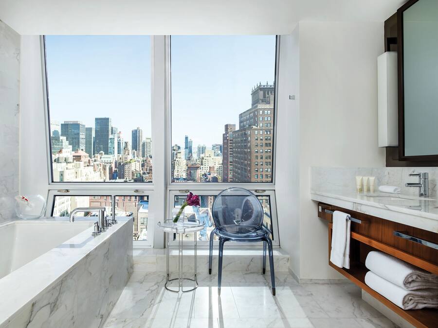A modern bathroom with a large window, a bathtub, a sink, and a chair.