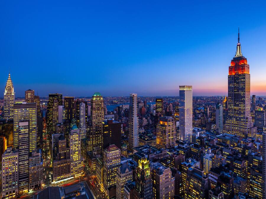 A cityscape at dusk with prominent skyscrapers, including the Empire State Building, and a dense urban environment.