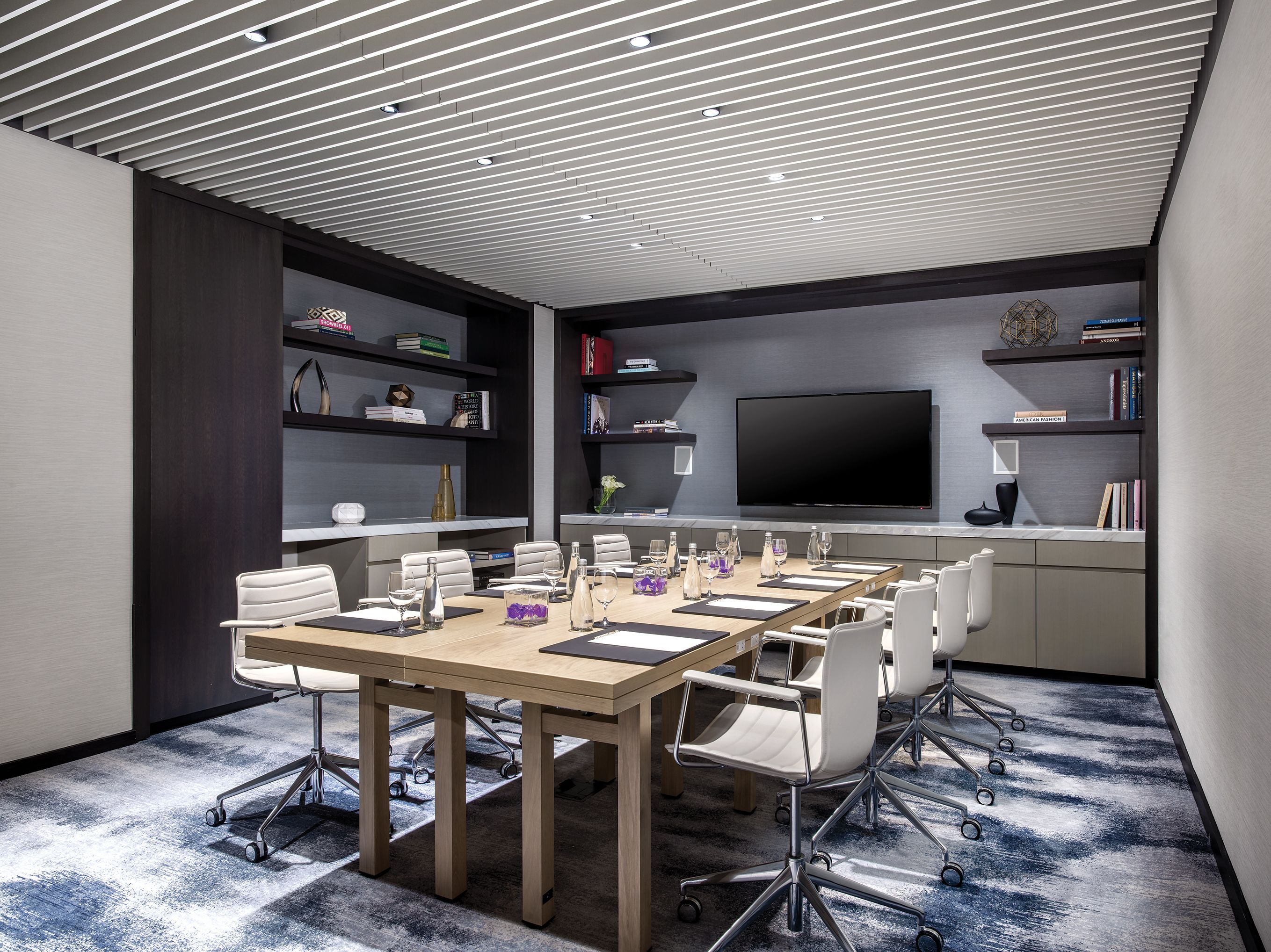A conference room with a large table, chairs, a TV, and bookshelves.