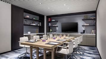 A conference room with a large table, chairs, a TV, and bookshelves.