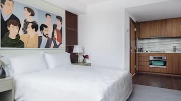 Ein Hotelzimmer mit einem großen Bett, einem Bild an der Wand, einem kleinen Tisch mit einer Lampe und einer Küchenzeile.