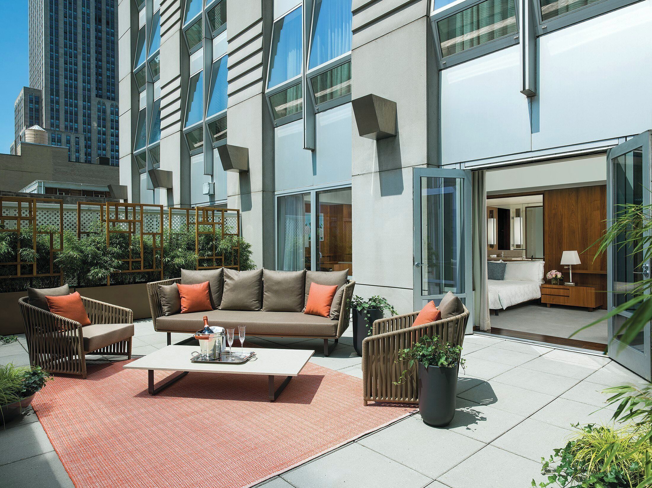 A modern outdoor seating area with a sofa, chairs, and a table, surrounded by potted plants and a decorative fence.