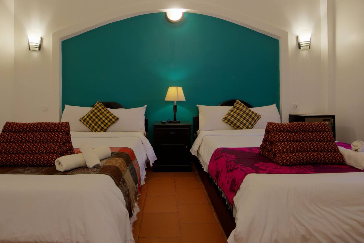 Een hotelkamer met twee bedden, een blauwgroen hoofdeinde en een nachtkastje met een lamp.