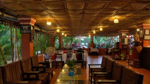 Un restaurant doté d’un toit de chaume, de meubles en bois et d’une longue table conviviale agrémentée d’une plante en guise de décoration centrale.