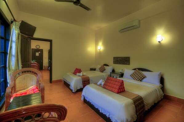Habitación de hotel con tres camas, ventilador de techo y vista al exterior.