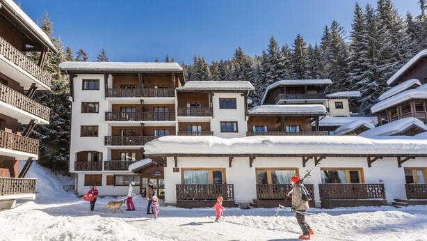 Un edificio cubierto de nieve con varios balcones y una pista de esquí al fondo.