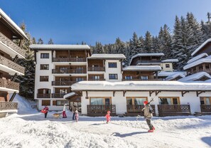 A snow-covered building with multiple balconies and a ski slope in the background. - Odalys Residence Front de Neige (Araches-la-Frasse)