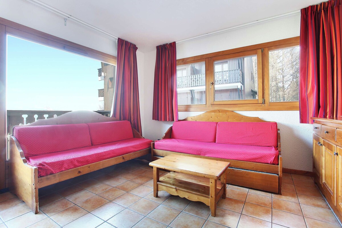 A cozy room with a wooden sofa, a small wooden table, and a window with curtains.