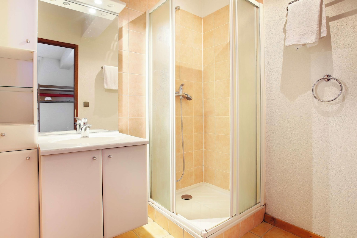 Un baño con ducha envuelta en vidrio, un lavamanos con espejo y un aro para toallas en la pared.