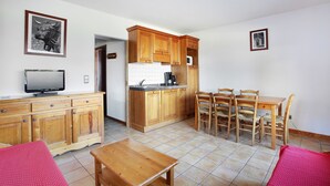Un espacio habitable compacto con kitchenette, comedor y televisor sobre un mueble de madera.