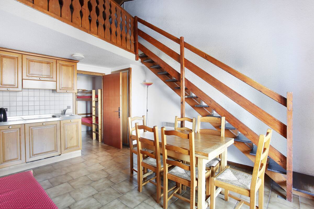 Una cocina con armarios de madera, una mesa de comedor con sillas y una escalera de madera.
