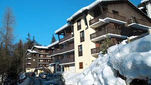 Un hotel de varios pisos con balcones, un telesilla y paisajes nevados.