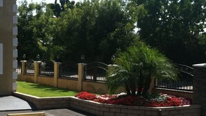 A landscaped area with a palm tree and red flowers, surrounded by a brick wall and metal gates. - Walnut Inn & Suites West Covina (West Covina)