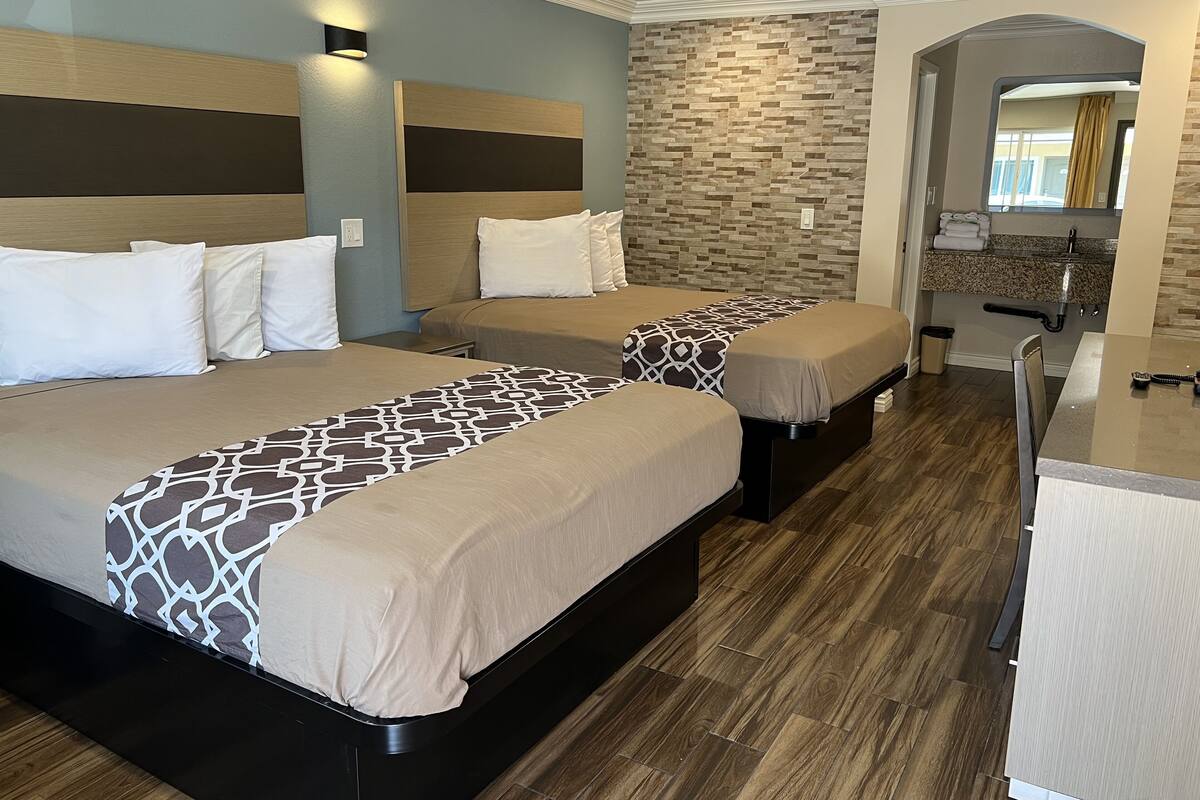 A hotel room with two beds, a small kitchenette, and a bathroom visible through an archway.