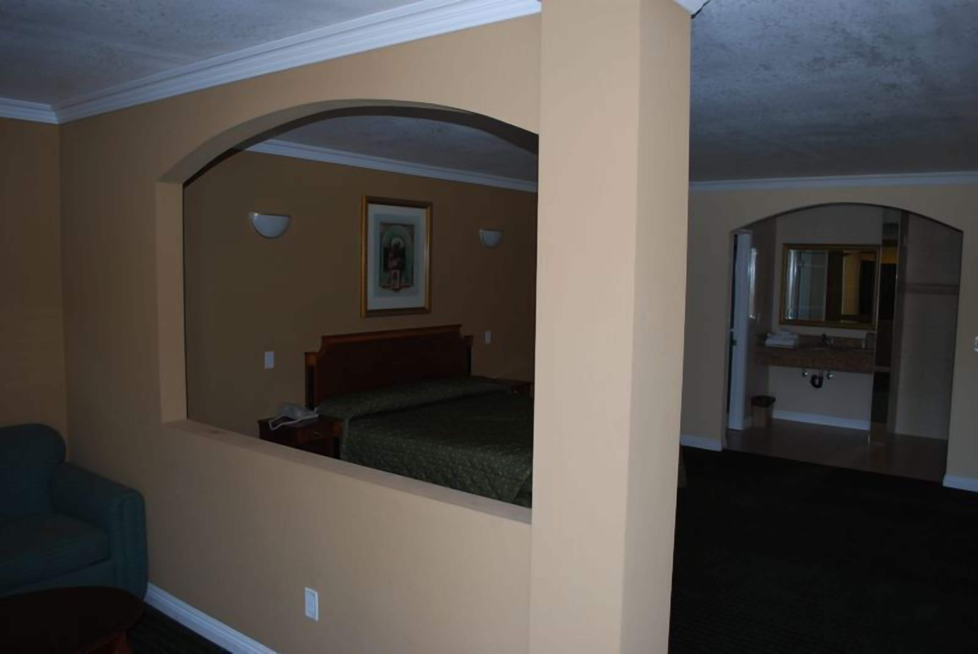 A hotel room with a bed, a chair, and a bathroom visible through an archway.