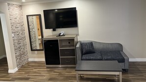 A living room with a flat-screen TV mounted on the wall, a grey sofa, a coffee table, and a wooden cabinet with drawers. - Walnut Inn & Suites West Covina (West Covina)