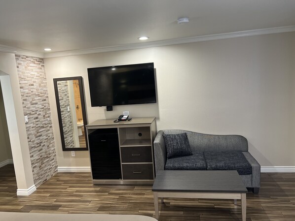 Una sala de estar con una televisión de pantalla plana montada en la pared, un sofá gris, una mesa de centro y un mueble de madera con cajones.