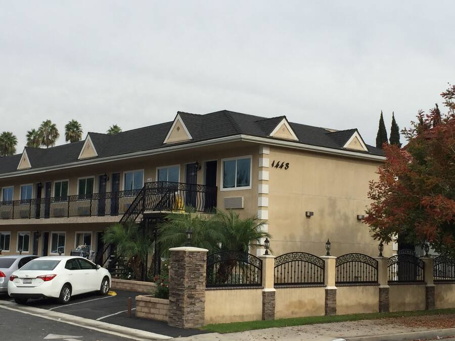 A multi-story hotel with a beige facade, numbered 1445, featuring balconies, a parking area, and a gated entrance.