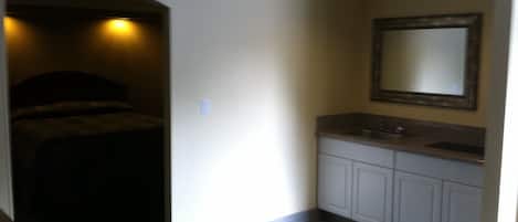 Un dormitorio con cama y un baño con lavabo y espejo.