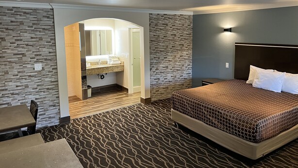 A hotel room with a bed, a bathroom with a vanity, and a patterned carpet. - Walnut Inn & Suites West Covina (West Covina)
