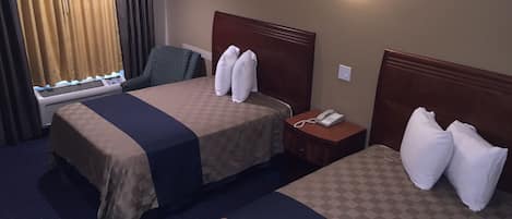 A hotel room with two beds, a desk, a chair, a phone, and a wall-mounted light.
