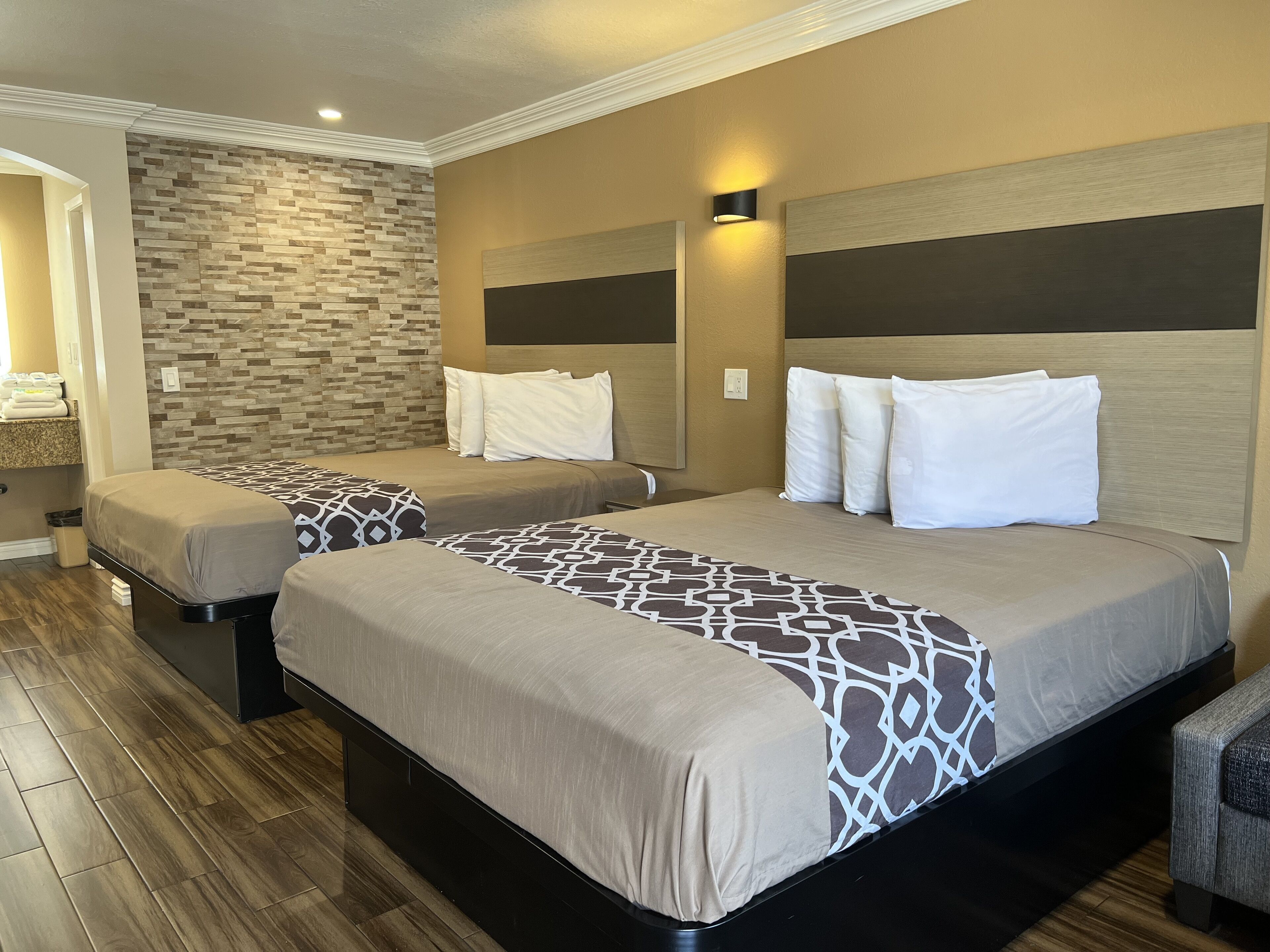 A hotel room with two beds, a stone wall, and a modern light fixture.