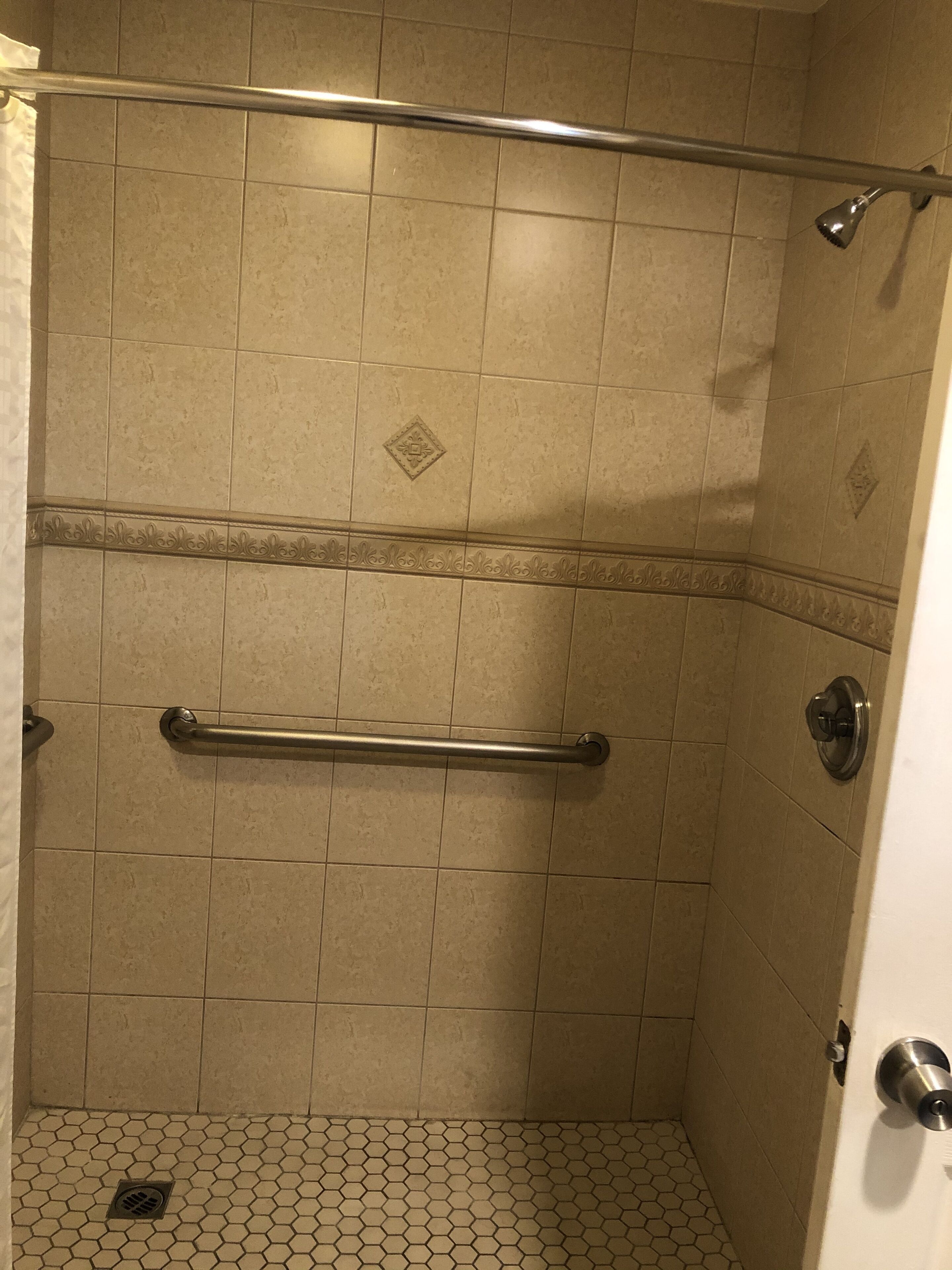 A shower with a handrail, tiled walls, and a hexagonal floor pattern.