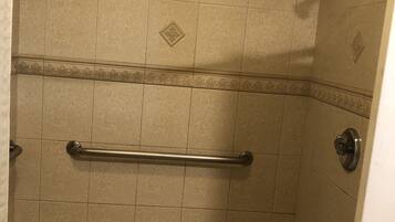 A shower with a handrail, tiled walls, and a hexagonal floor pattern.