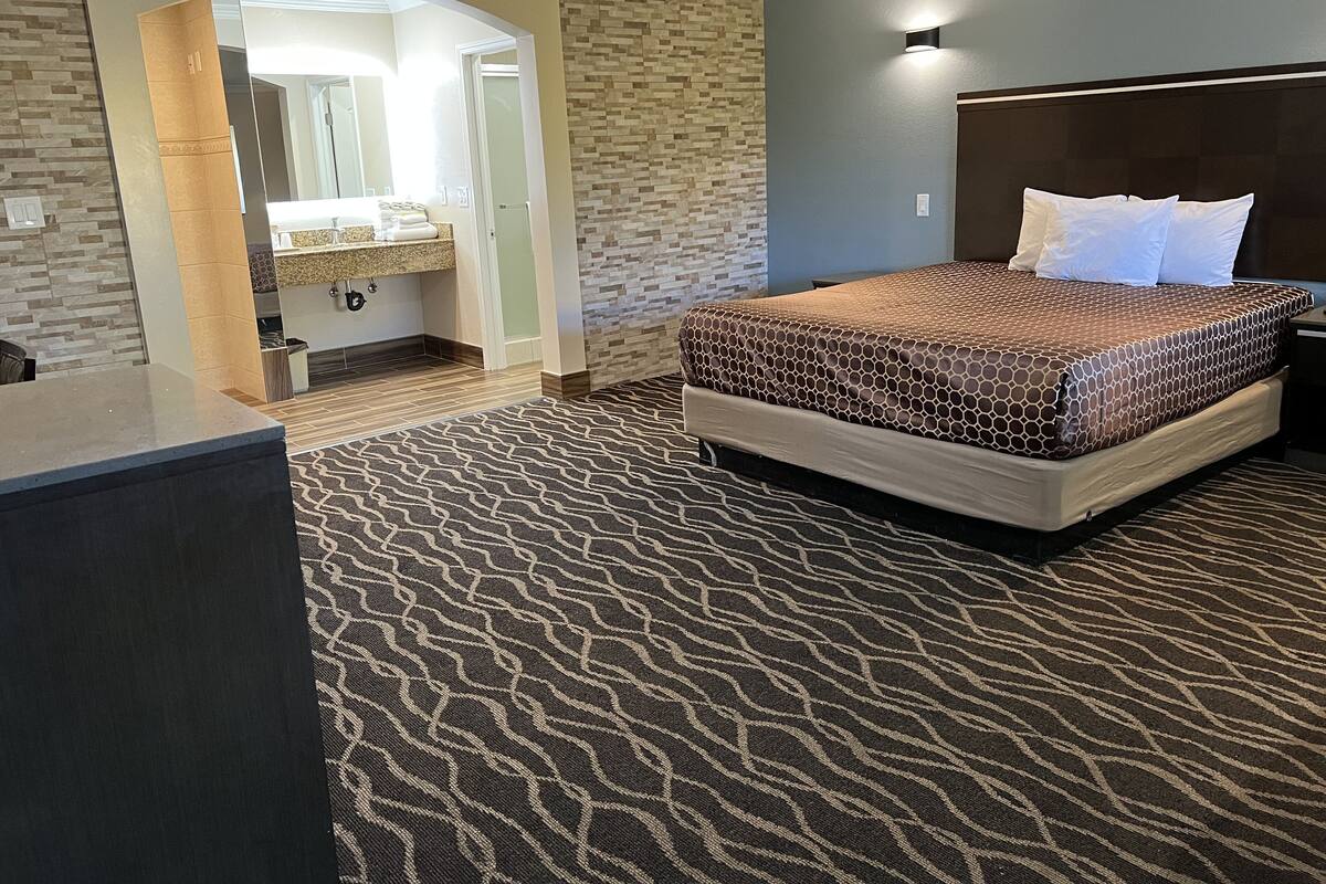 A hotel room with a bed, a desk, and a bathroom visible through an archway.