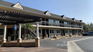 A multi-story hotel with a covered entrance, a handicap parking sign, and a clear sky. - Walnut Inn & Suites West Covina (West Covina)