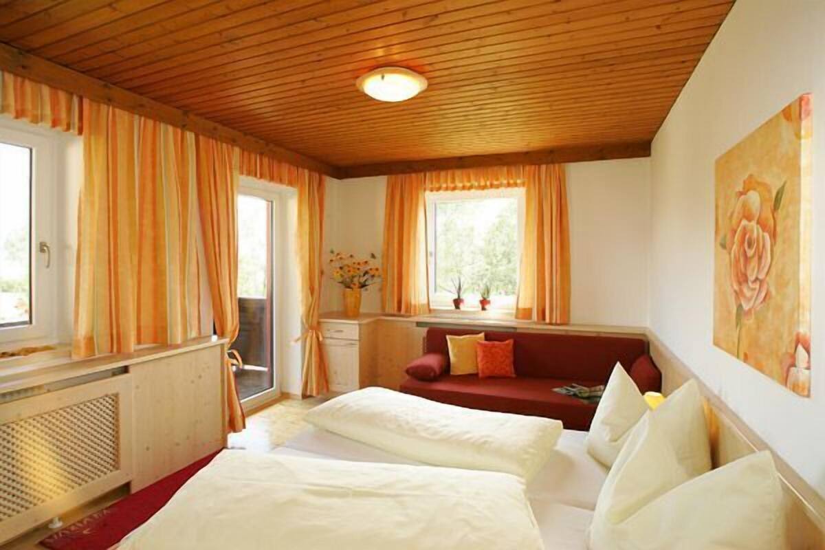Un dormitori amb dos llits, un sofà vermell, una finestra amb cortines i un quadre a la paret.