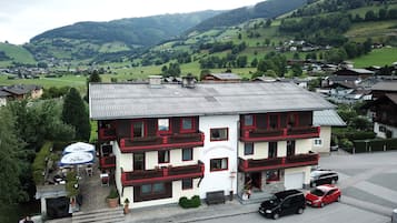 Ein Hotel mit weißer Fassade und roten Akzenten, gelegen in einer gebirgigen Gegend mit sichtlicher Vegetation und weiteren Gebäuden im Hintergrund.